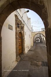 Image du Maroc Professionnelle de  Dans une rue des Habous, la succession des balèvres, moulure, arches, portiques et autres éléments décoratifs, projetent les visiteurs dans l’ardeur avec un élan de force et de fierté d’une époque révolue. Conçu par les architectes Auguste Cadet et Edmond Brion d’après l’ébauche d’un premier plan-masse dû à Albert Laprade, le quartier fait partie des endroits les plus pittoresques de Casablanca, il fut La construction n’avait commencé qu’après la première guerre mondiale. Situé près du Palais Royale, ce joyau architectural fait partie du patrimoine architectural de la ville, Samedi 8 Novembre 2008. Au centre le minaret de La mosquée Ben Youssef. (Photo / Abdeljalil Bounhar)
